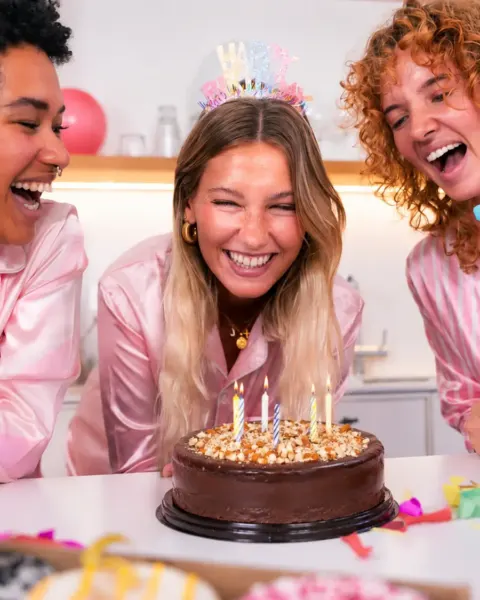 Amigas en pijama celebrando con torta y velas